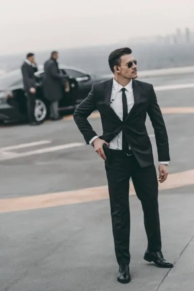 Professional executive bodyguard in a formal suit providing discreet personal security near a luxury vehicle at an airport.